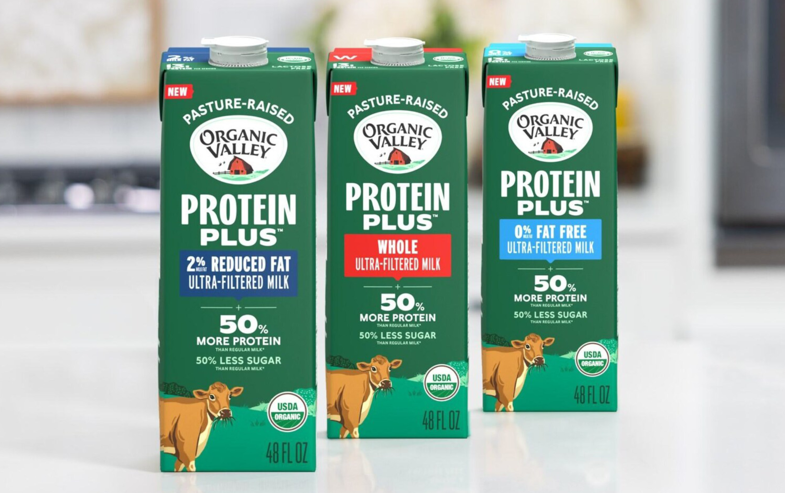 New Arrivals: Three cartons of Organic Valley Protein Plus ultra-filtered milk—2% reduced fat, whole, and 0% fat free—feature 50% more protein and 50% less sugar. Each carton displays a cow image at the bottom.