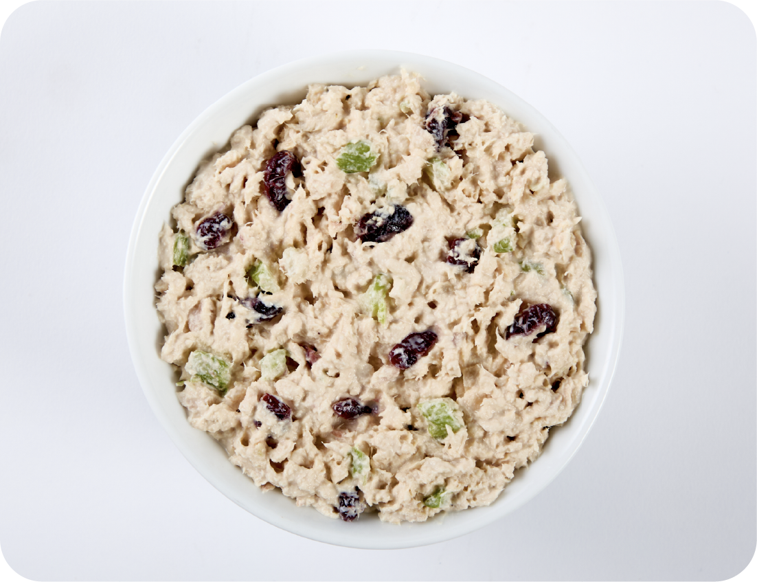 A white bowl filled with chicken salad—chunks of chicken, green celery pieces, and dried cranberries—set against a plain white background, perfect for a refreshing bite at your next Seafood Event.
