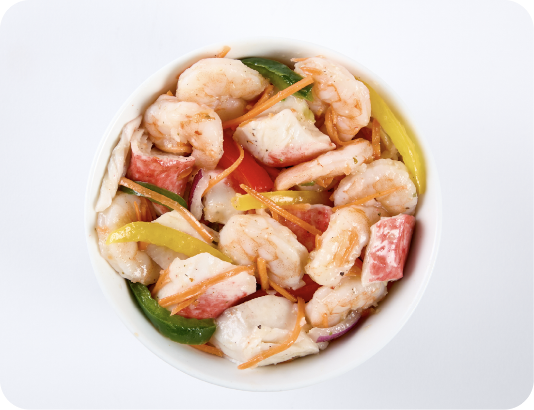A Seafood Showcase: a bowl of seafood salad featuring shrimp, imitation crab, sliced bell peppers, carrots, and green vegetables, all mixed together on a white background.