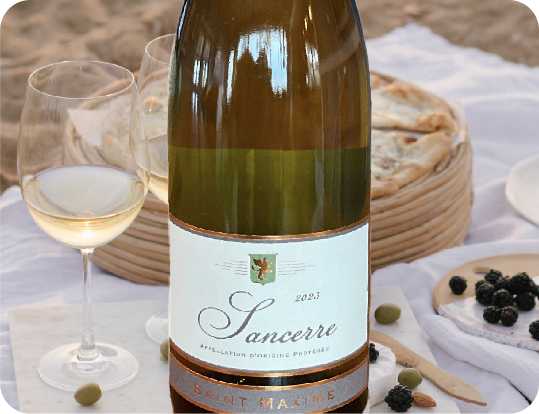 A bottle of Sancerre white wine stands on a table with a glass of wine, a pie, blackberries, green olives, and bread—perfect for pairing at any Seafood Showcase, set outdoors on a white tablecloth.