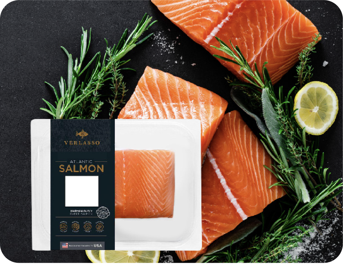 A package of Verlasso Atlantic salmon is displayed in front of fresh salmon fillets, lemon slices, rosemary, and sage on a dark surface for an appealing seafood showcase.