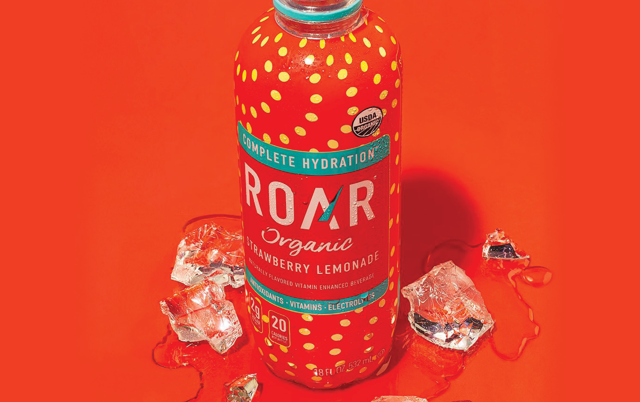 A red bottle of ROAR Organic Strawberry Lemonade drink stands on a red surface with ice cubes around it. The bottle is decorated with yellow dots and clear labeling, emphasizing hydration and organic ingredients.