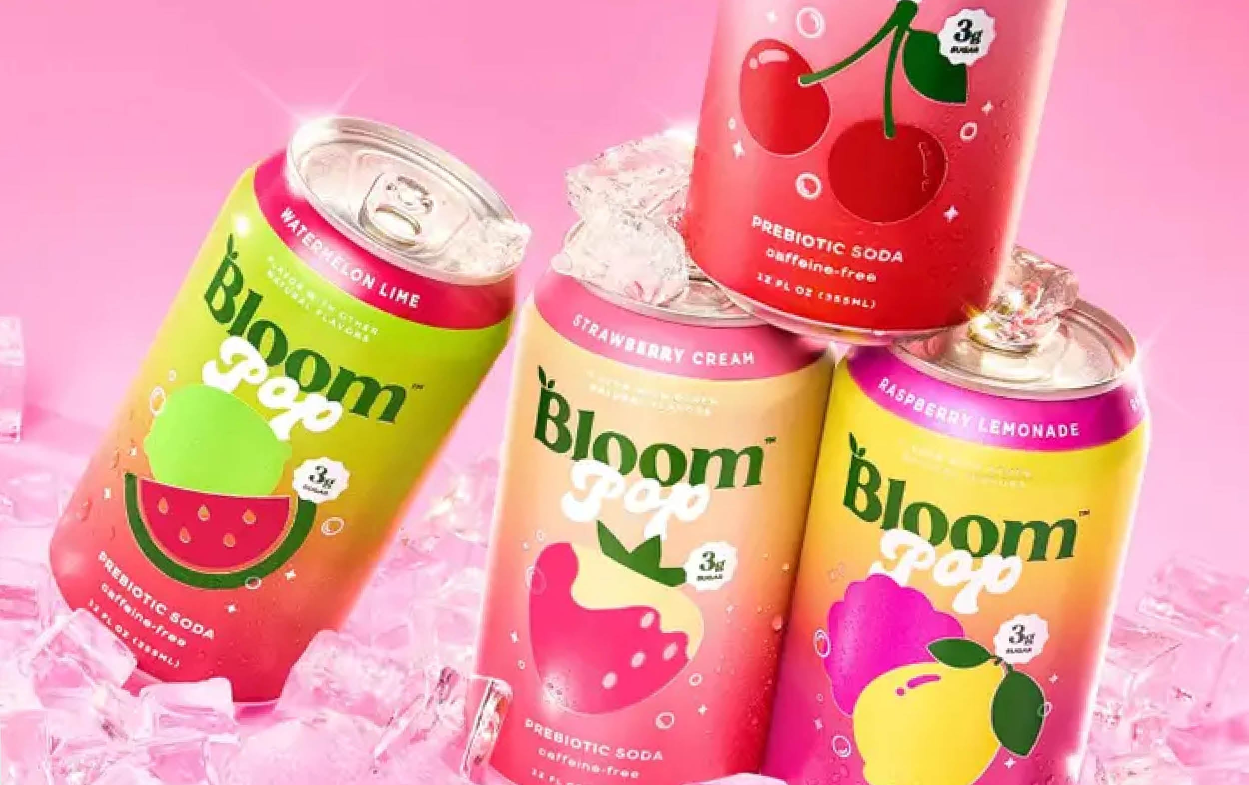 Four colorful Bloom Pop prebiotic soda cans in watermelon lime, strawberry cream, cherry, and raspberry lemonade flavors rest on ice against a pink background. Each can features fruit illustrations matching its flavor.